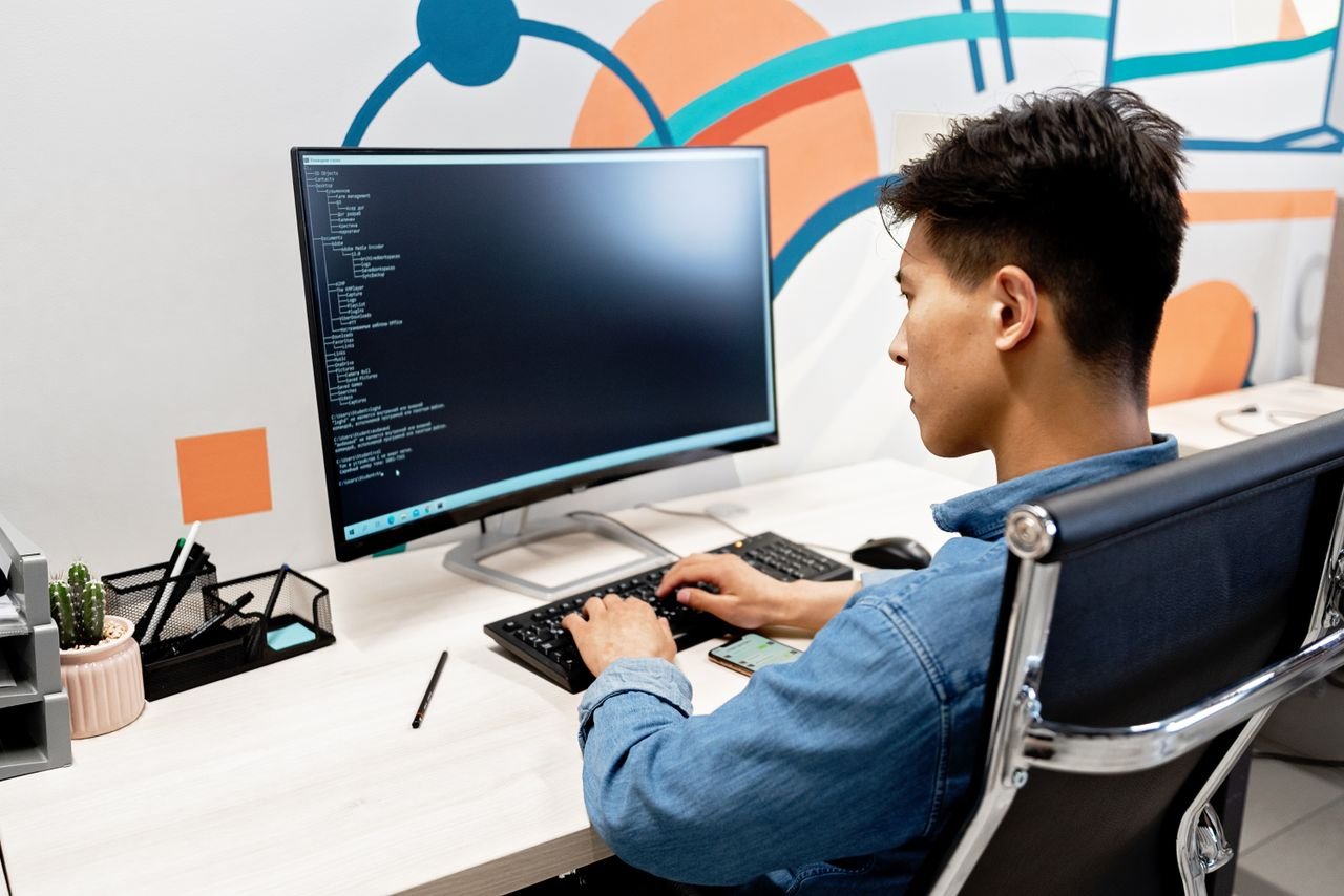 Home Adult male programmer working on code at a modern desk setup with a large monitor.